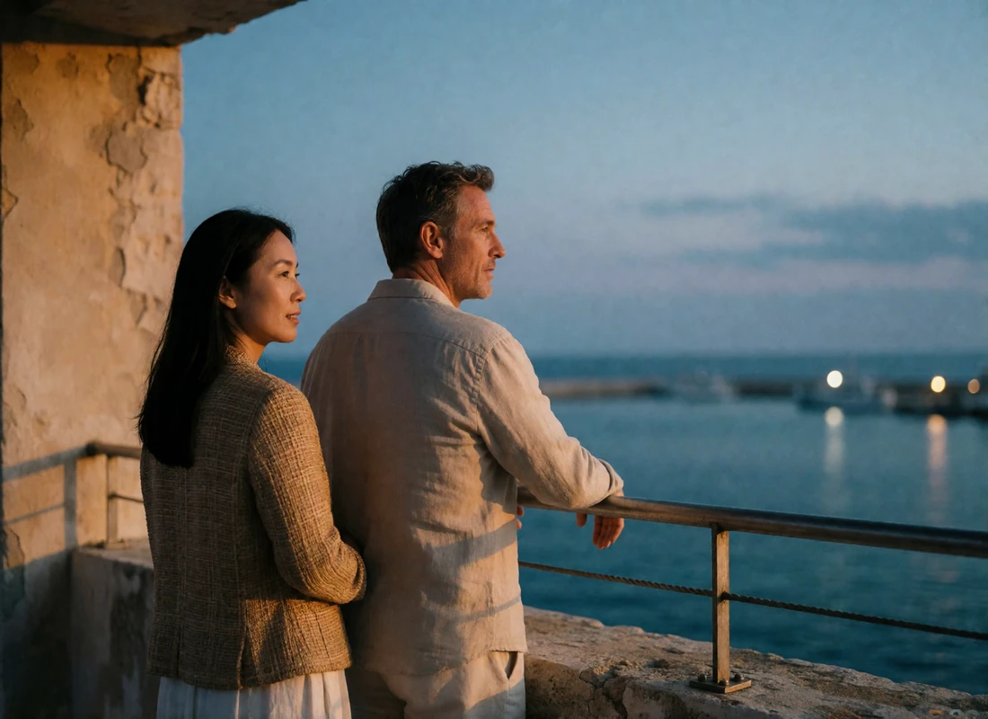 Asian woman and Western man standing side by side at a coastal rooftop railing at dusk